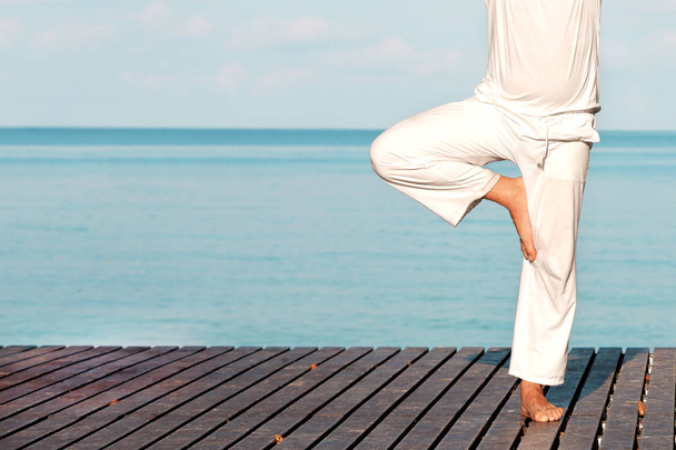 Man in white clothes meditating yoga on wooden pier - Fotoğraf, Görsel