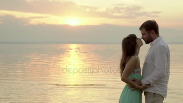 Felice giovane coppia in piedi sulla spiaggia al tramonto. Fidanzata bacio suo fidanzato
. - Filmati, video