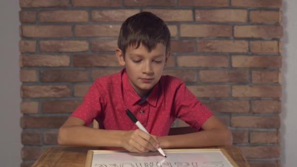 kind zit op het Bureau houden van flip-over met belettering handtekening op de achtergrond rode bakstenen muur. - Video