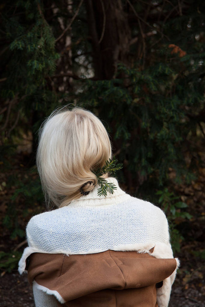 Mädchen, das mit dem Rücken im Wald steht. ihr warmer weißer Pullover macht es gemütlich und der Hintergrund aus Fichte verleiht dem Betrachter Weihnachtsstimmung. - Foto, Bild