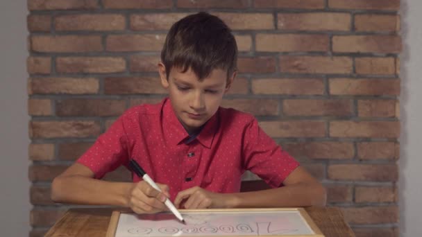 παιδί κάθεται στο γραφείο κρατώντας πινακάκι με επιγραφή εκατομμύρια στον τοίχο κόκκινο τούβλο φόντο. - Πλάνα, βίντεο