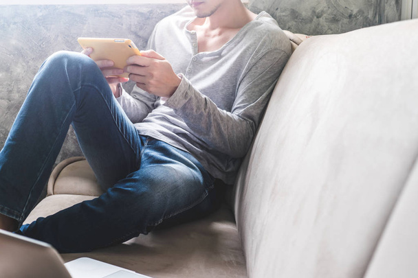Casual young man using tablet on sofa at home. - Photo, Image