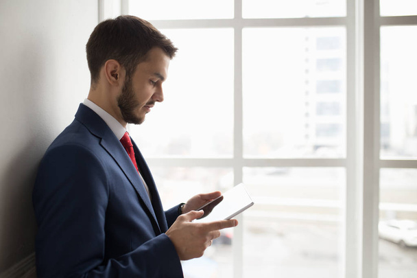 Businessman in white office using digital tablet at window - Zdjęcie, obraz