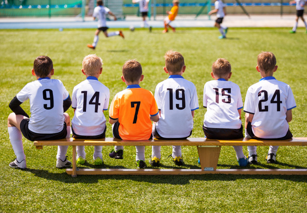 Nuoret jalkapalloilijat. Nuori jalkapallojoukkue istuu puisella penkillä. Jalkapallo ottelu lapsille. Nuoret pojat pelaavat turnauksen jalkapallo ottelu. Nuorten jalkapalloseura Jalkapalloilijat
 - Valokuva, kuva
