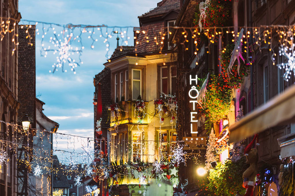 Otel neon işaret üstünde romantik lüks renkli Noel pazarı atmosfere Noel oyuncaklar ve en eski Noel pazarı dünya çapında, Strasbourg süslemeleri ile ışıklı cadde üzerinde yürüyen insanlar siluetleri ile bina - Fotoğraf, Görsel