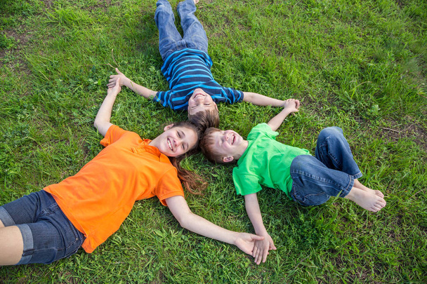 Three happy kids lying down on green grass - Foto, Imagem