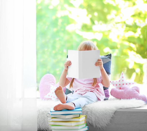 Beautiful little girl with book on windowsill - Foto, Imagem