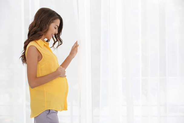 pregnant woman standing near window at home - Photo, image