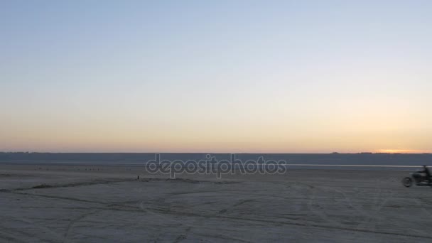 Tres motociclistas cabalgando cerca de la playa de arena en el desierto lejos durante el atardecer
. - Metraje, vídeo