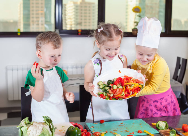 Drie schattige kinderen zijn de voorbereiding van een salade in de keuken - Foto, afbeelding