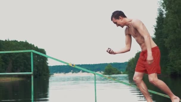 Young man running to water at lake with go pro camera in hands. Summer. Emotions - Materiał filmowy, wideo