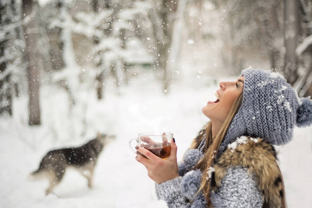 Chica disfruta de las caídas de nieve. Mujer joven en forma de punto está bebiendo té en el bosque durante una nevada. Foto tonificada
 - Foto, Imagen