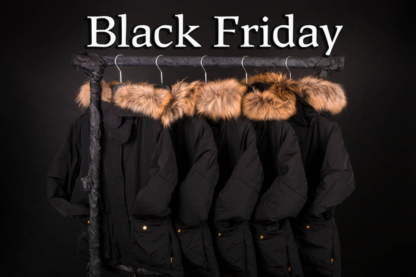 Schwarzer Freitag. viele schwarze Mäntel, Jacke mit Pelz auf Kapuze, die auf Kleiderständern hängt - Foto, Bild
