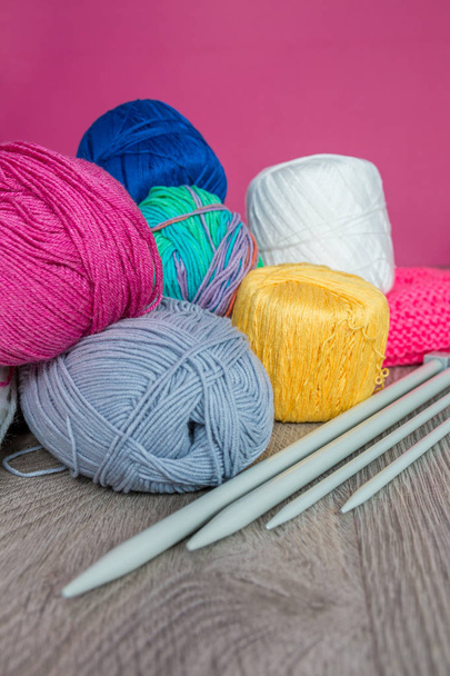 編み物。糸とグレーの木製テーブル ピンク背景に針のグループ。手作り。クローズ アップ. - 写真・画像
