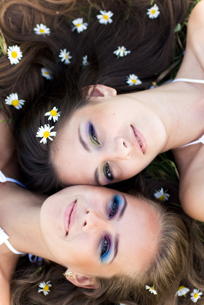 Dos hermosas mujeres tumbadas cabeza a cabeza con flores de manzanilla en
 - Foto, imagen
