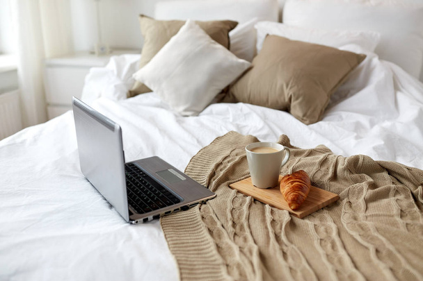 laptop, coffee and croissant on bed at cozy home - Foto, afbeelding