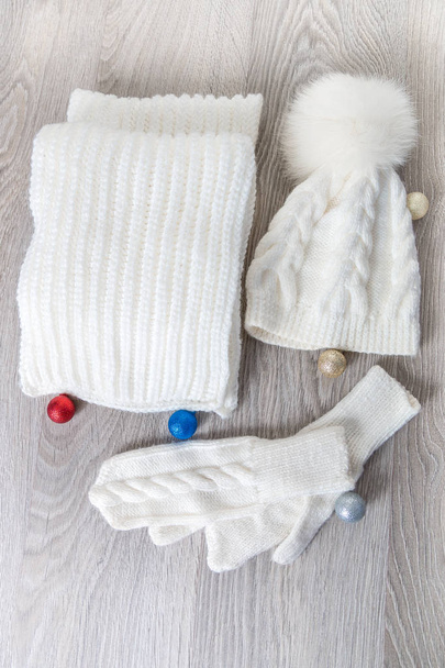 Příslušenství pro pletené chladné počasí poblíž novoroční strom koule na stole. Bílý klobouk, šátek ant rukavice šedé dřevěné pozadí. Pohled shora. Vánoční dekorace. - Fotografie, Obrázek