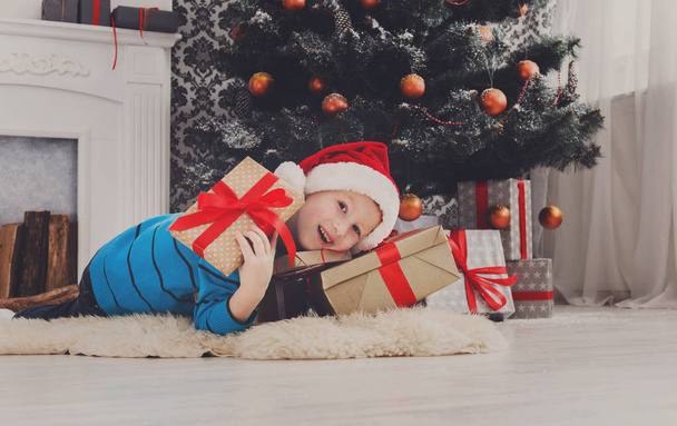 menino bonito em santa chapéu desembrulhando presentes de Natal
 - Foto, Imagem