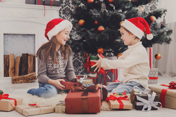 Szczęśliwe dzieci w santa kapelusze rozpakowaniu świątecznych prezentów - Zdjęcie, obraz