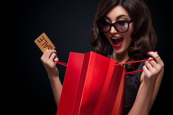 Happy woman open red bag on dark background in black friday holiday - Photo, Image