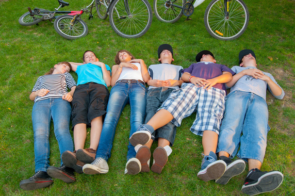 Підлітки хлопчики і дівчатка лежать в траві після їзди на велосипедах
 - Фото, зображення