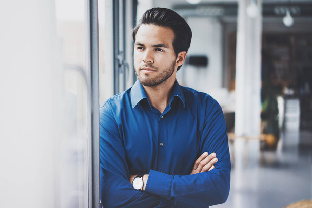 Portrait of successful confident hispanic businessman standing close from the window in modern office.Horizontal,blurred background. - 写真・画像