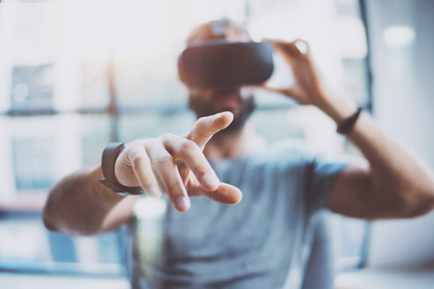 Closeup of male hand.Bearded young man wearing virtual reality goggles in modern coworking studio. Smartphone using with VR headset in office. Horizontal, blurred. - Fotoğraf, Görsel