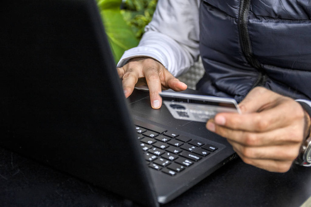 Man holding credit card in hand and entering security code using laptop keyboard. Young businessman holding a credit card and typing. On-line shopping on the internet using a laptop - Zdjęcie, obraz