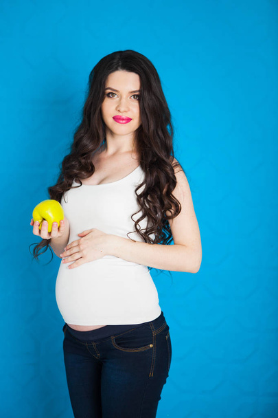 Pregnant happy young woman with green apple on blue background,  - Foto, imagen