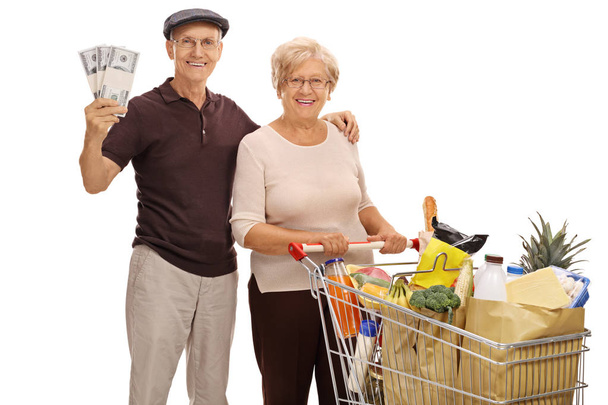 seniors with money bundles and shopping cart full of groceries - Foto, imagen