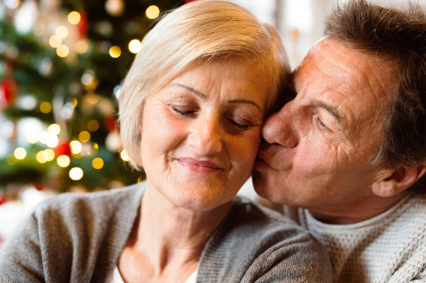 Senior couple in front of Christmas tree kissing, close up. - Foto, imagen