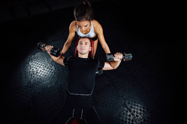 Γυναικεία προσωπική fitness εκπαιδευτή βοηθώντας έναν νεαρό άνδρα στο γυμναστήριο. - Φωτογραφία, εικόνα
