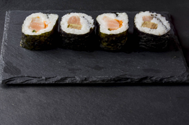 Stukken van sushi op een zwarte steen - Foto, afbeelding