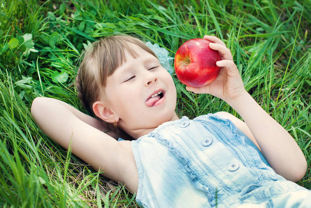 Hezká dívka jíst červené jablko na louky a pastviny. Šťastné děti koncept. - Fotografie, Obrázek