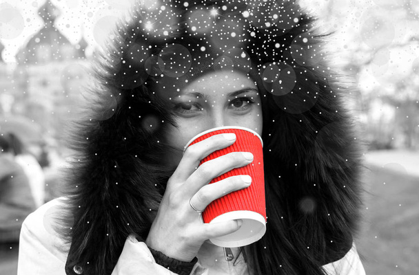 Yound girl drinks a red cup of hot tea black and white filtered with shiny snowfall - Photo, Image