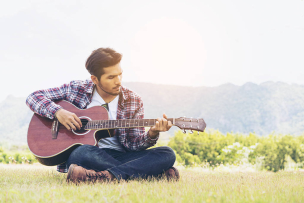 Όμορφος άντρας παίζει κιθάρα στο πράσινο γρασίδι - Φωτογραφία, εικόνα