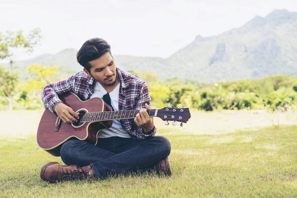 Bonito homem tocando guitarra na grama verde
 - Foto, Imagem