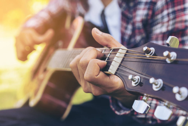 Man 's hand playing guitar, sitting on green grass - Photo, Image
