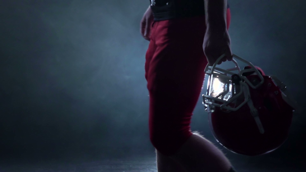 Football is a red helmet in his hand. Black background. Slow motion - Footage, Video