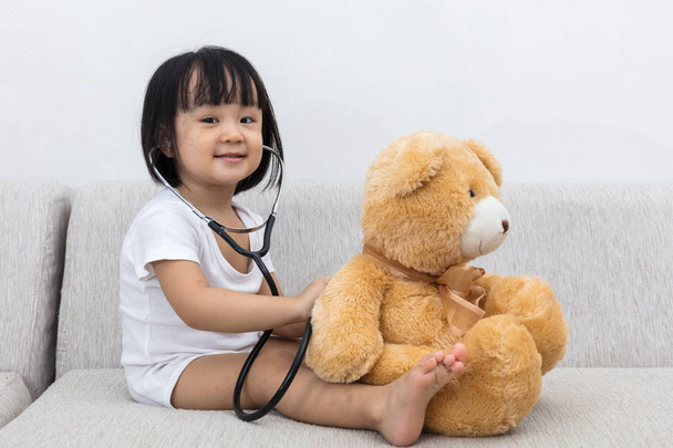 Asian Chinese little girl checking up a teddy bear - Fotó, kép
