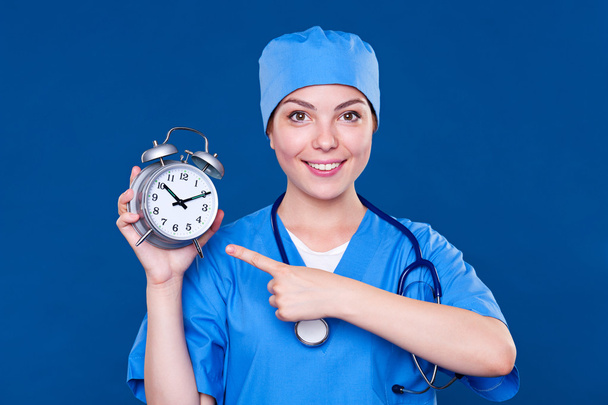 smiley nurse pointing at alarm clock - Photo, Image