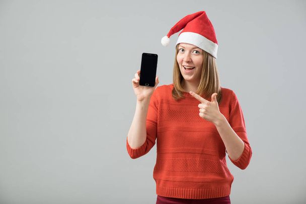Young  woman with Santa hat showing smartphone - Fotó, kép