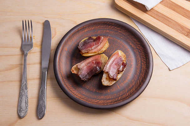 Baked potatoes with slices of bacon on wooden background. - 写真・画像