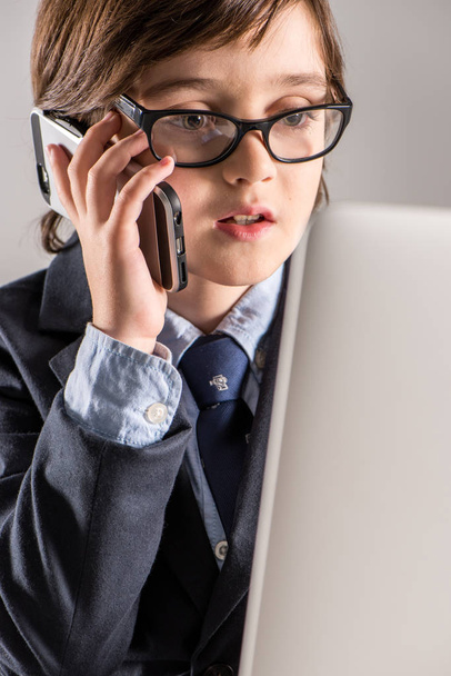 Niño de escuela en traje de negocios hablando por teléfono inteligente
 - Foto, Imagen