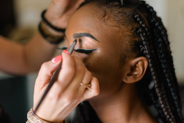 Make up of american black model. Preparing to shooting. Closed eyes. Braiding - Фото, изображение