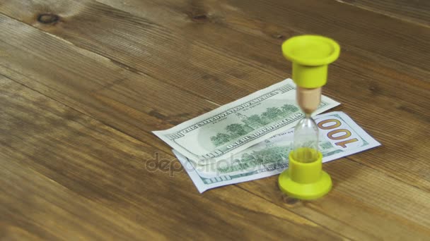 Dollar biljetten vallen op een houten tafel en de zandloper - Video