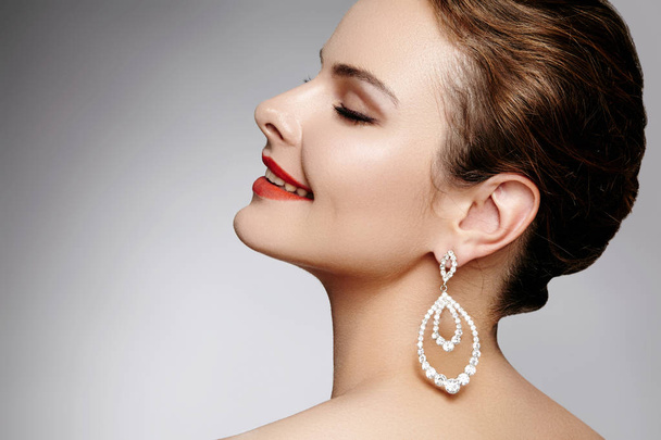 Beautiful happy woman in luxury fashion earrings. Diamond shiny jewelry with brilliants. Sexy retro style portrait. Model with glamour accessories jewelery and bright red lips makeup - Fotoğraf, Görsel