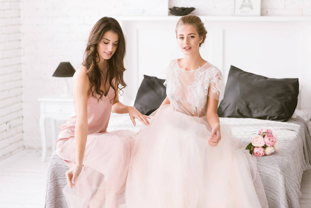 Delighted bride and bridesmaid sitting in the white room - Фото, изображение