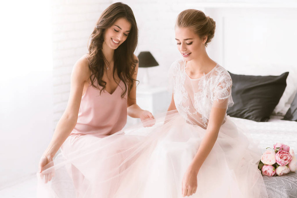 Smiling bride and bridesmaid sitting on the bed - Фото, зображення