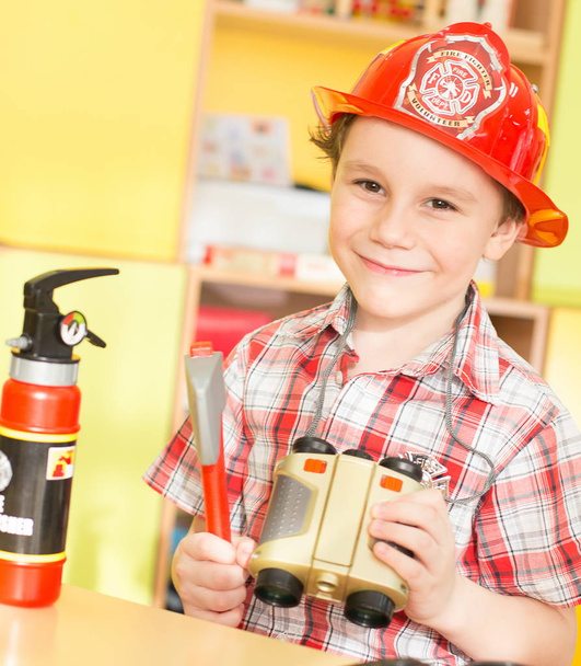 cheerful smiling boy with toys and binoculars in his hands in a fire suit - Photo, Image